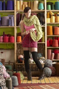 1239318-768920-young-woman-knitting-scarf-standing-in-front-of-yarn-display